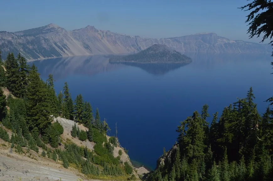 A view of Crater Lake with tiny evergreen tree lining the ledge