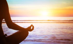 Person practicing yoga on the sandy beach at sunrise, with gentle ocean waves in the background.